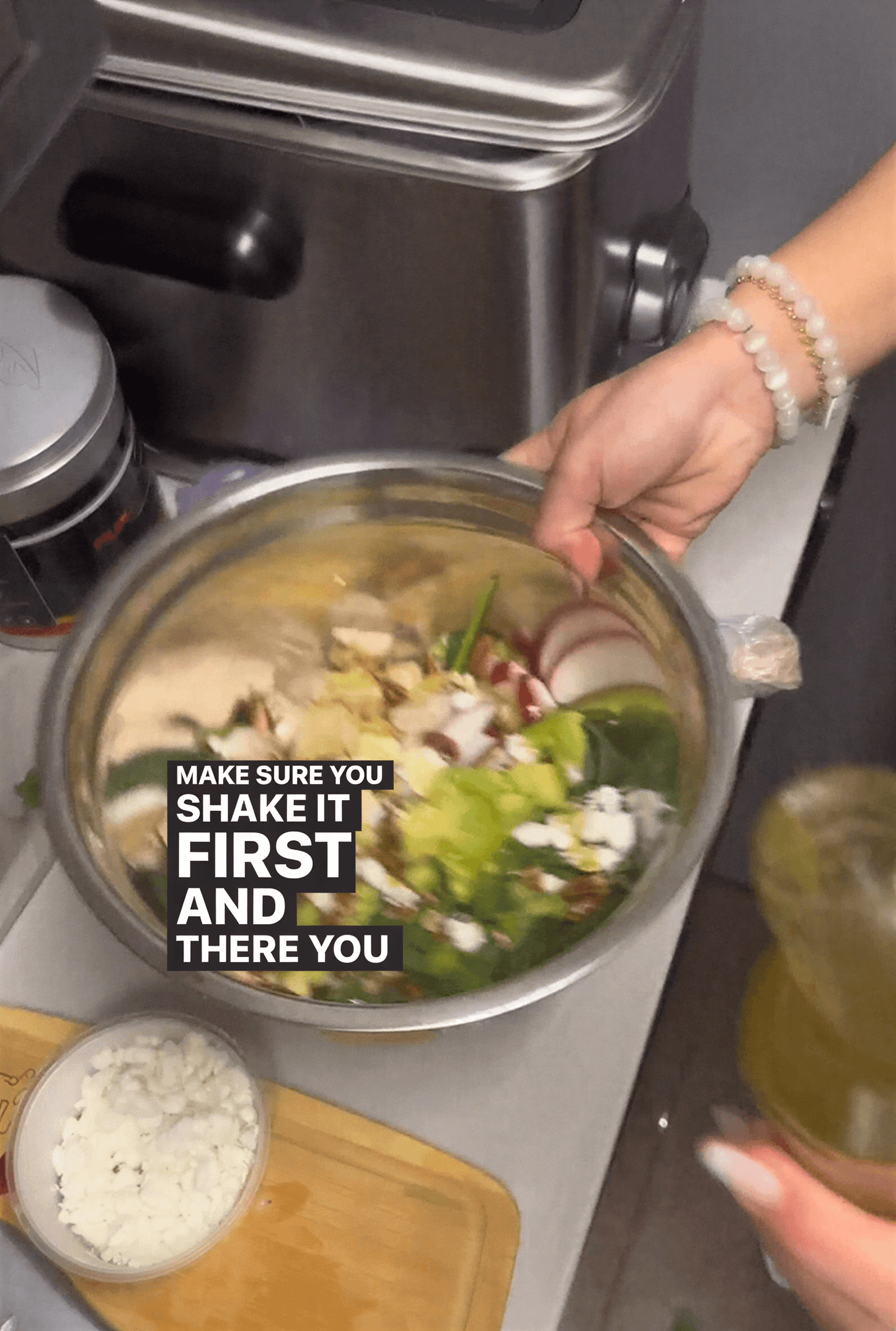 A person holding a metal bowl filled with chopped vegetables, with a bottle of dressing nearby on a kitchen counter.