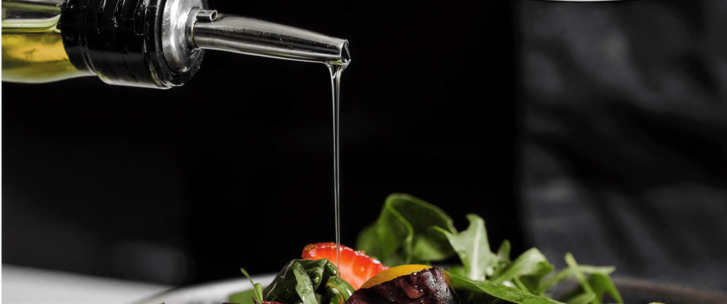 Stainless steel oil pour spout dispensing oil over a fresh salad with greens and sliced strawberries.